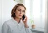 988 at Four Years: 23 Million Contacts and a Funding Model That Has Not Caught Up An adult talking on a smartphone beside a window in a bright room.