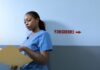 Emergency Departments Can Start Buprenorphine. Most Opioid Visits Still End Without It. A nurse in blue scrubs reading a patient chart in a hospital corridor.