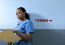 Emergency Departments Can Start Buprenorphine. Most Opioid Visits Still End Without It. A nurse in blue scrubs reading a patient chart in a hospital corridor.