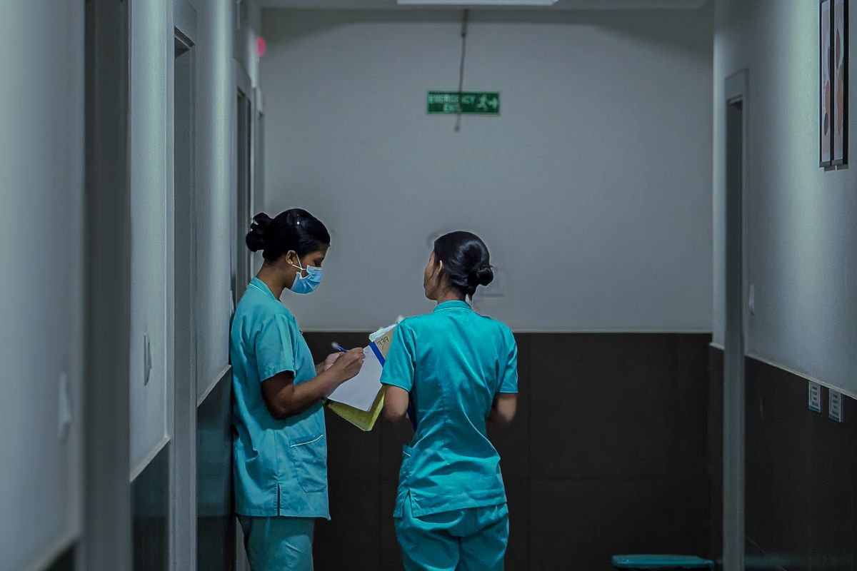 Two hospital clinicians in scrubs reviewing a patient chart together in a hospital corridor