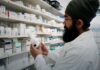Naloxone Went Over the Counter Three Years Ago. Price and Shelf Placement Still Decide Who Gets It. Shelves of packaged medicines behind a pharmacy counter.