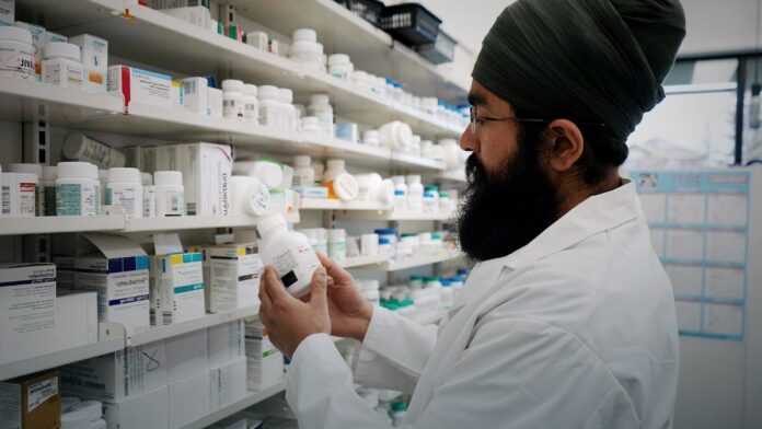 Shelves of packaged medicines behind a pharmacy counter.
