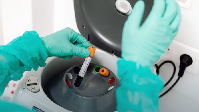 A gloved laboratory worker handles sample vials during testing.