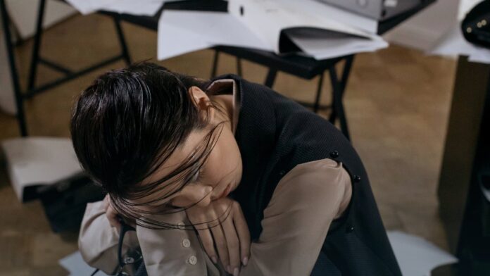 A person sitting with head lowered, appearing exhausted and unwell.
