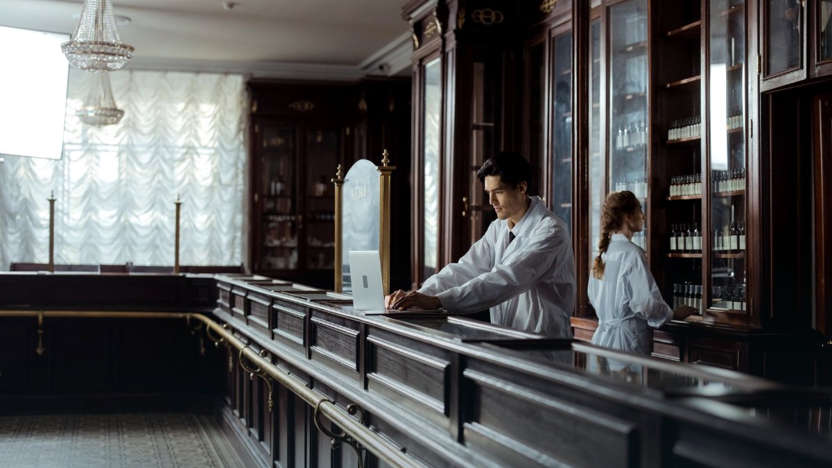 A pharmacist working behind a counter with shelves of medication.